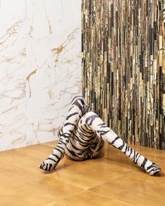 Artistic picture of a woman laid down on the floor with her legs crossed in a leopard design legging in front of a two connection wall where each one of the walls has a different Roberto Cavalli tile.