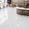 Modern café interior with polished 48x48 Statuarietto porcelain tile flooring and matching Statuarietto tile countertop, featuring subtle grey veining and a glossy white finish.